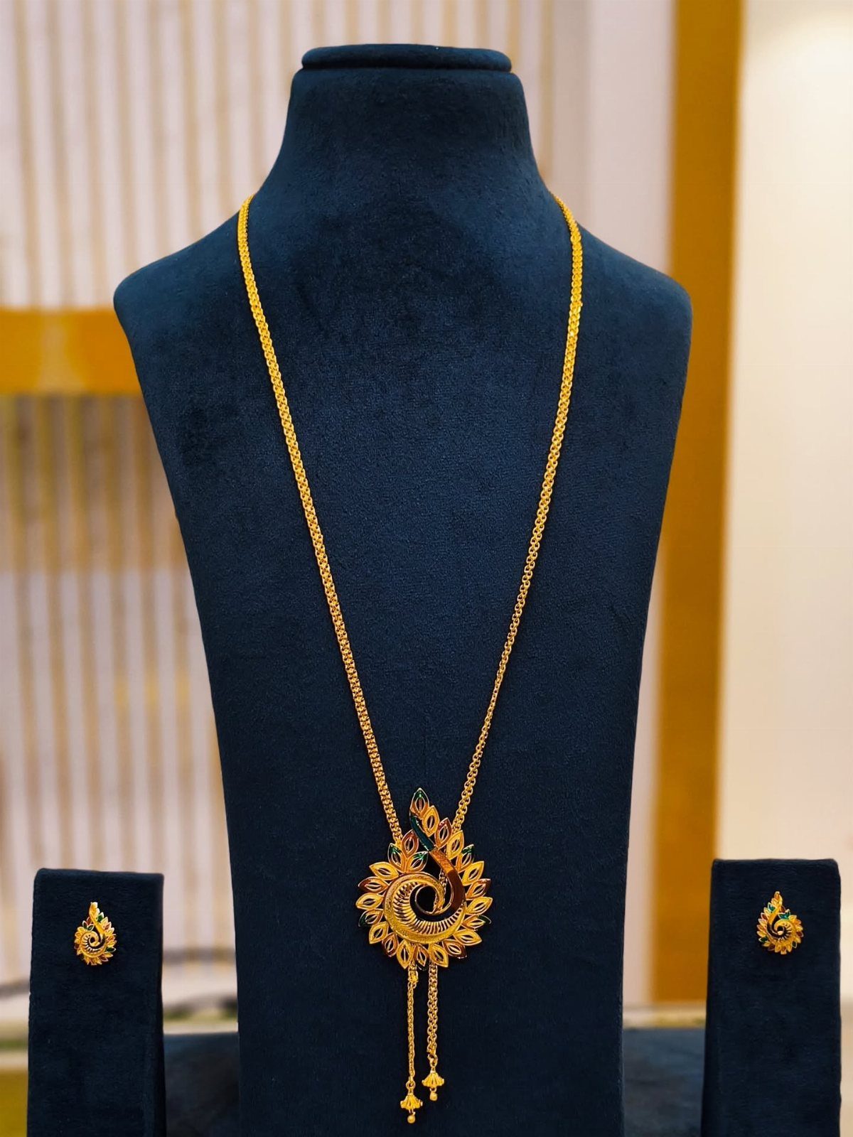Gold necklace with a detailed peacock motif pendant displayed on a dark blue velvet jewelry bust.
