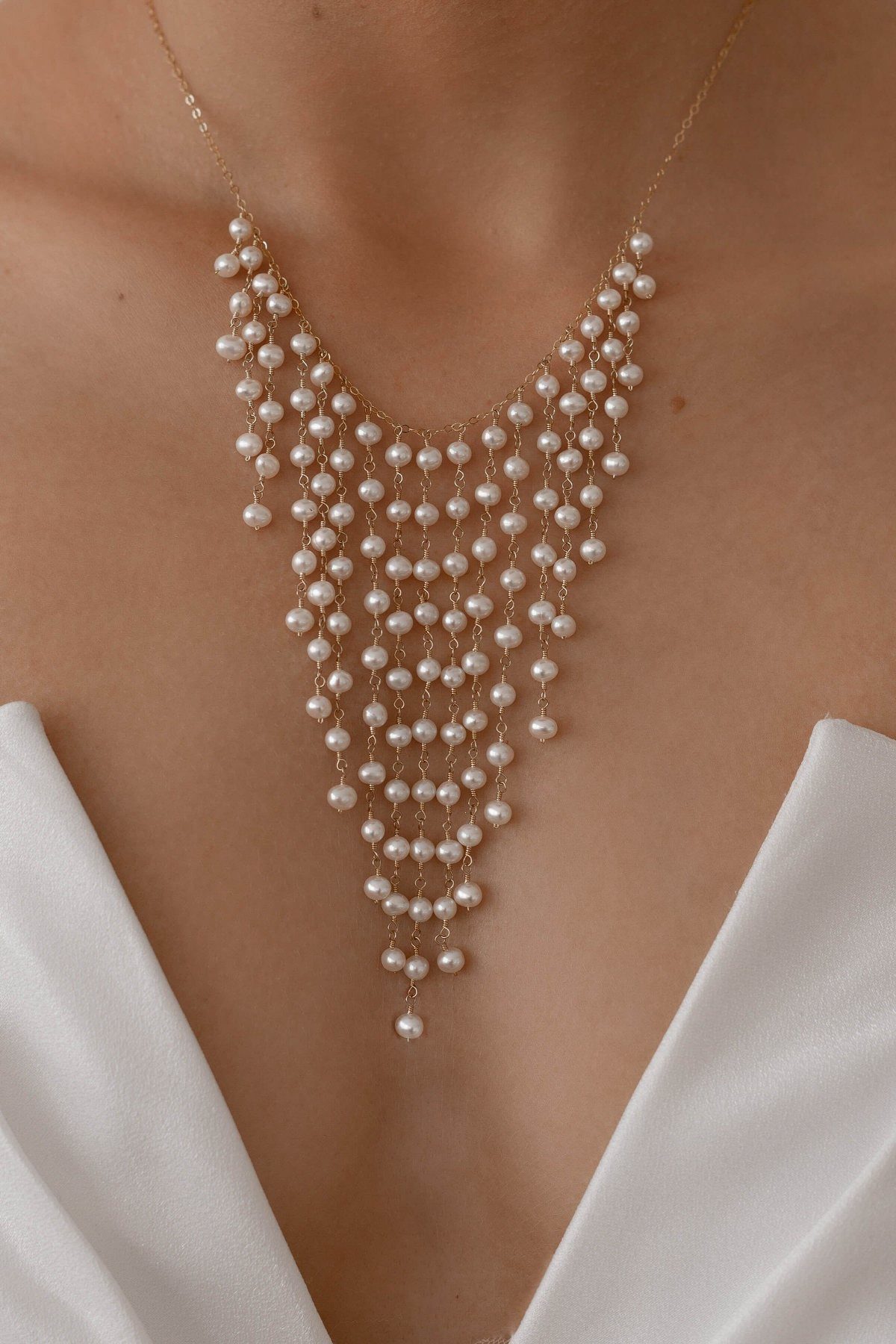 A gold necklace with multiple cascading layers of white pearl drops worn by a person.