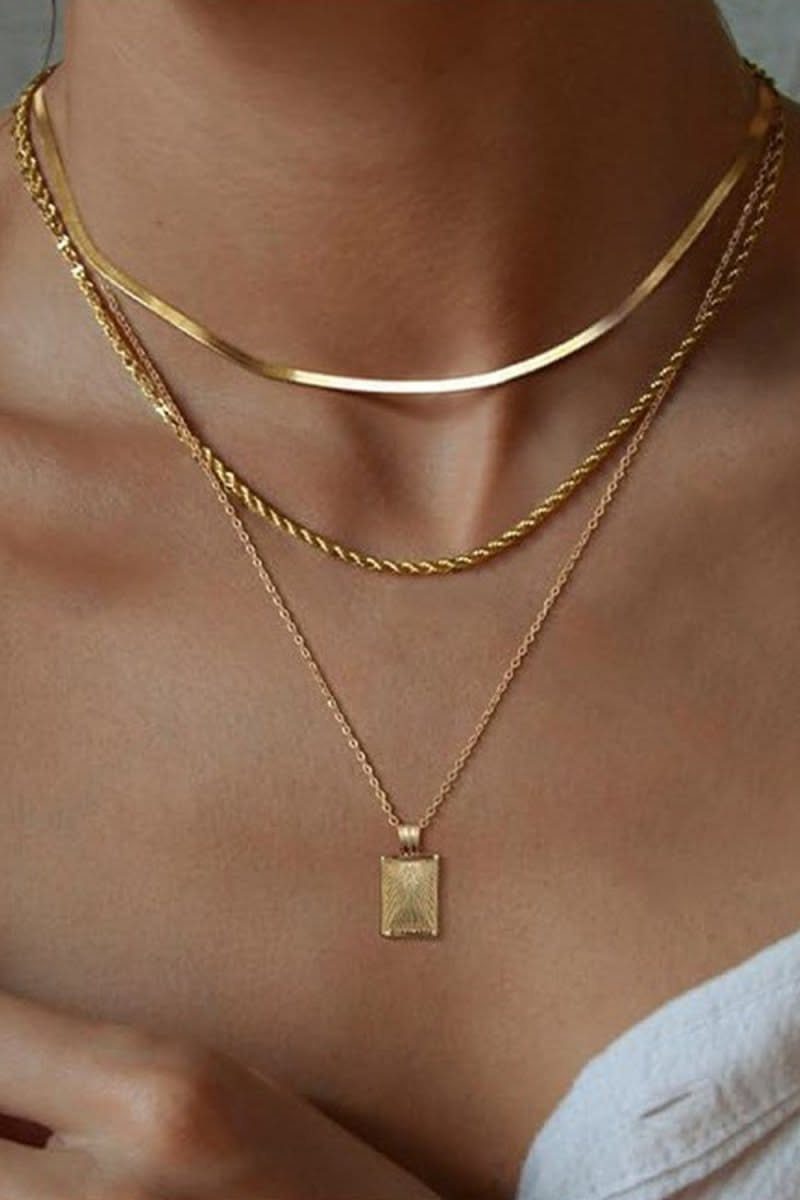 Three layered gold necklaces of varying textures and lengths worn on a person's neck.