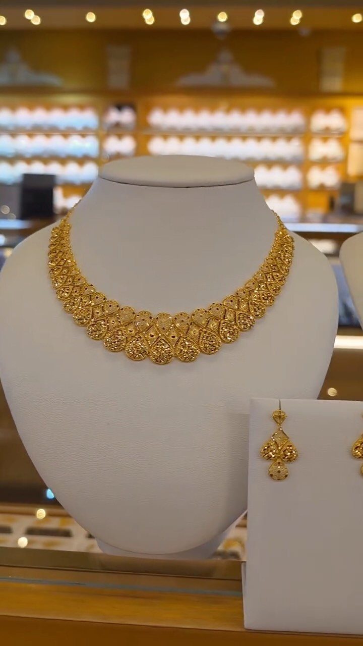 Gold necklace and matching earrings displayed on white jewelry busts in a store.