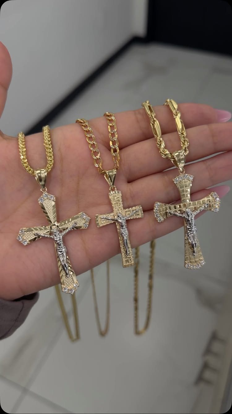 Three gold cross necklaces with various intricate designs held in a person's hand.