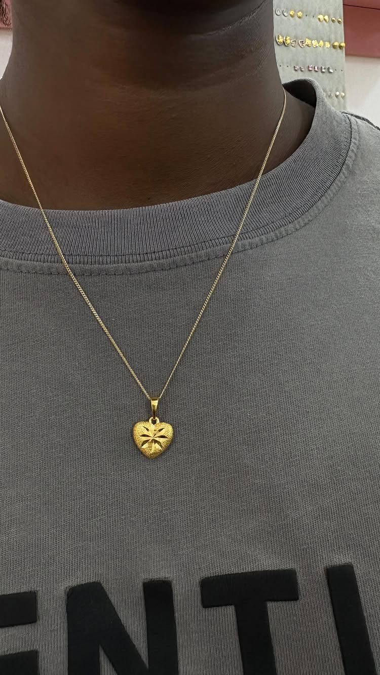 A gold heart-shaped pendant on a thin chain worn over a grey shirt.