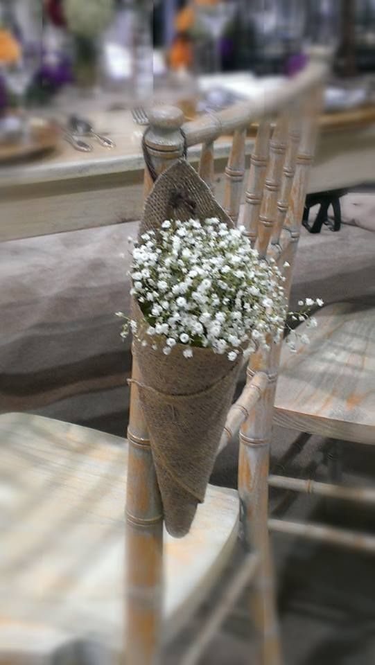 Baby's breath flowers wrapped in a burlap cone hanging on a wooden chair back.