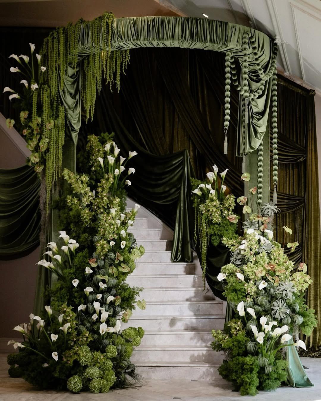 White calla lilies and green foliage decorating a grand staircase with dark green fabric draping.