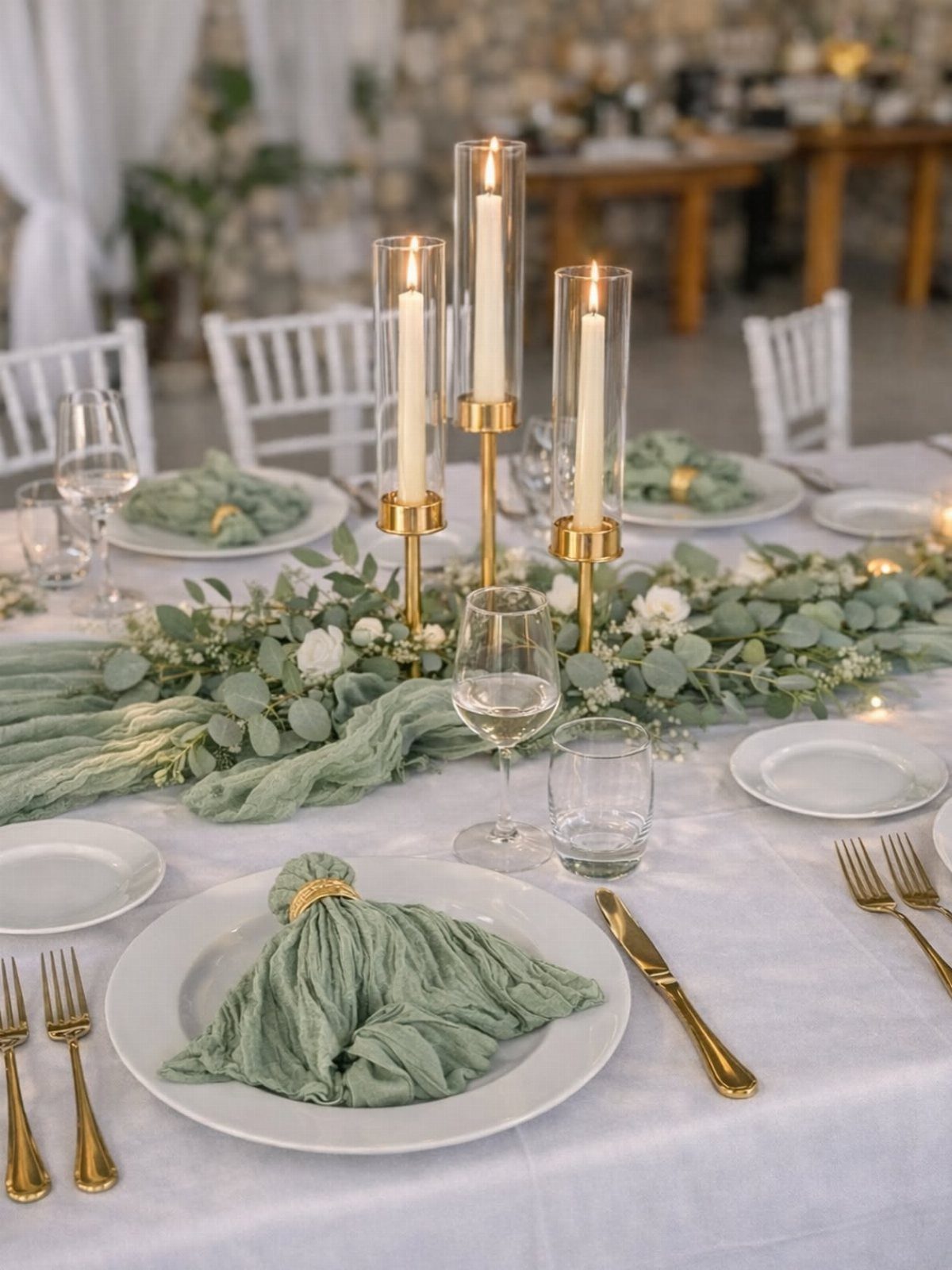 Eucalyptus greenery and white flowers decorate a wedding table with sage green napkins and gold cutlery.