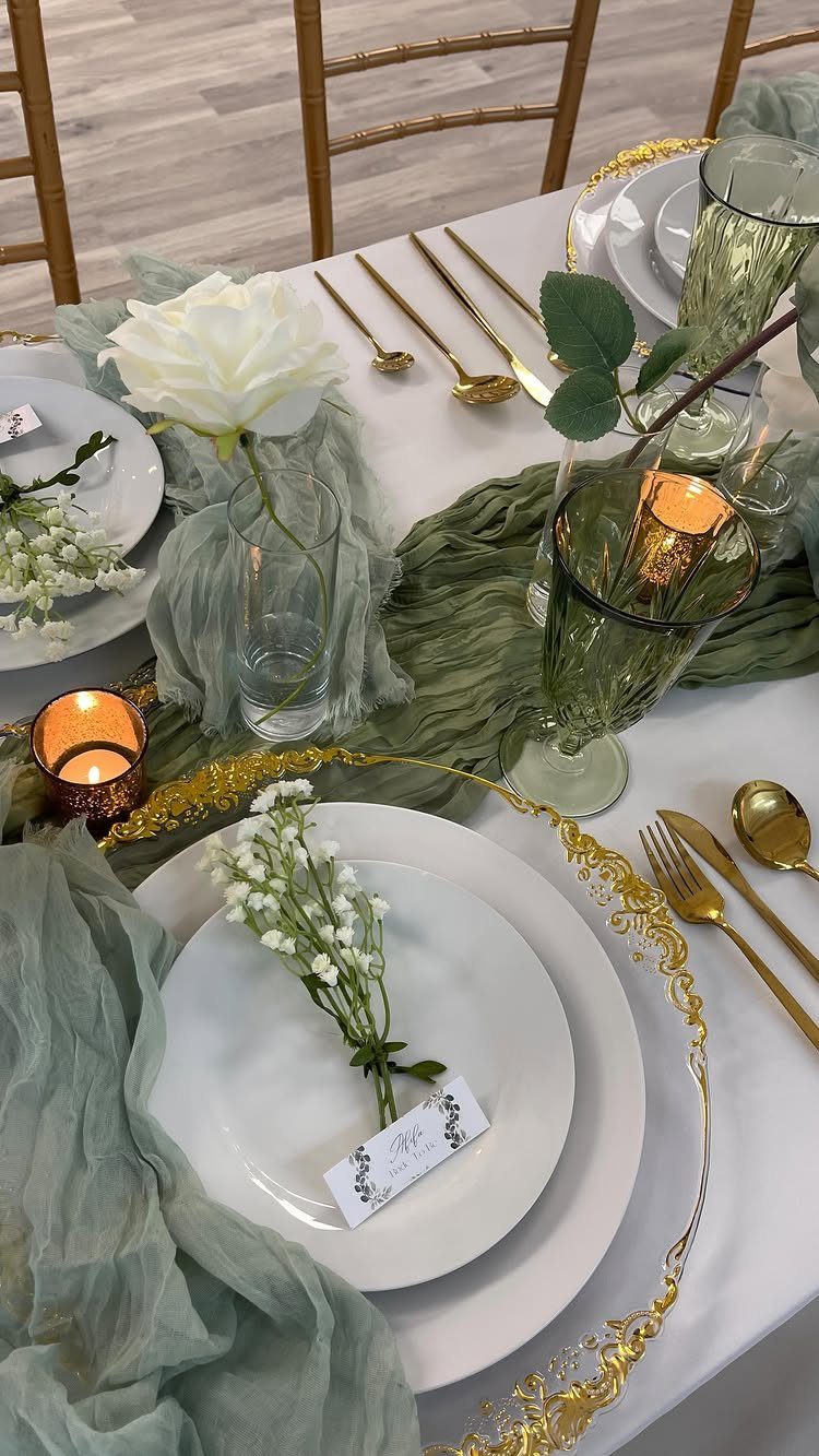 White plates with gold cutlery and sage green fabric runners on a wedding table.