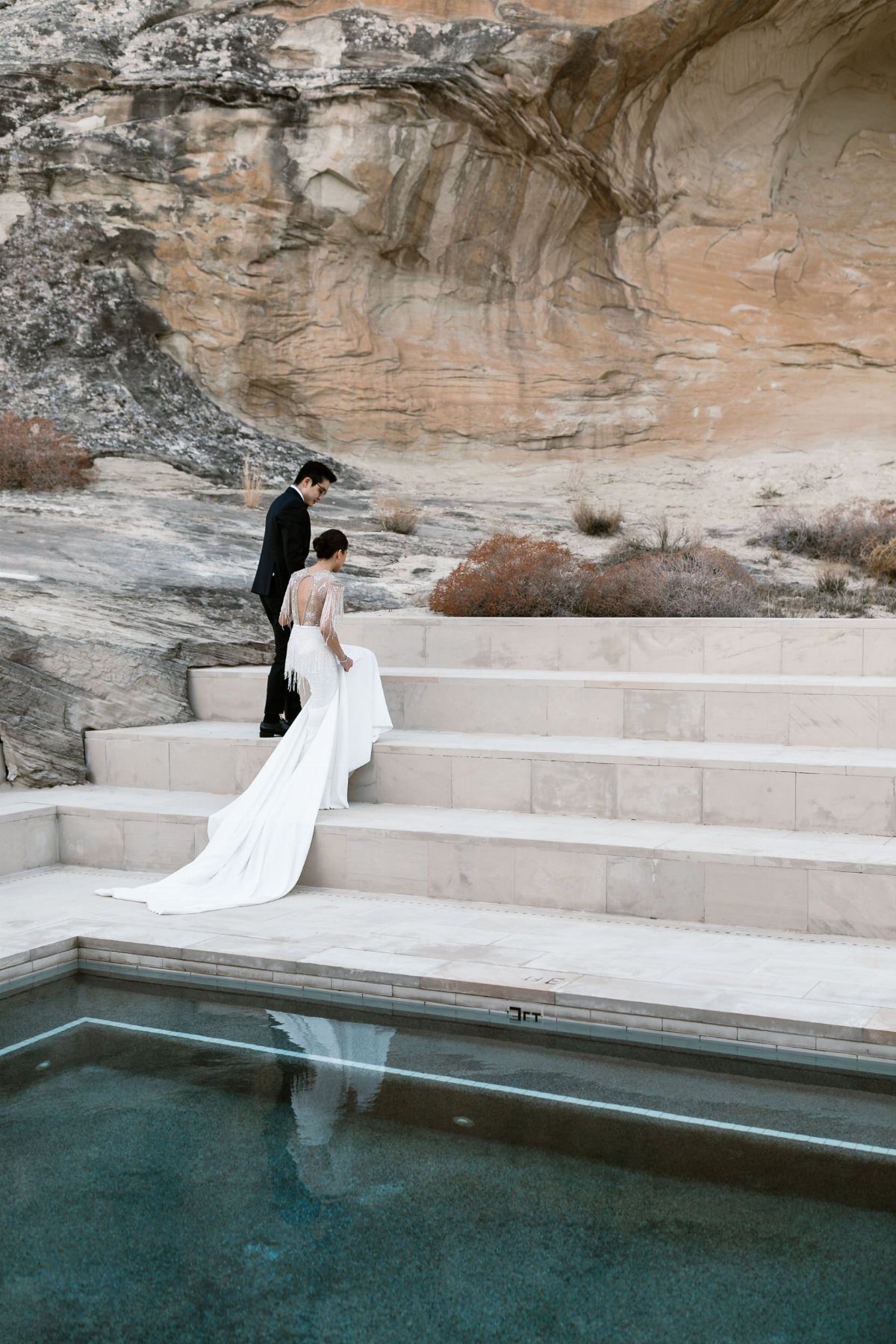A bride and groom walking up wide stone steps against a massive desert rock cliff.