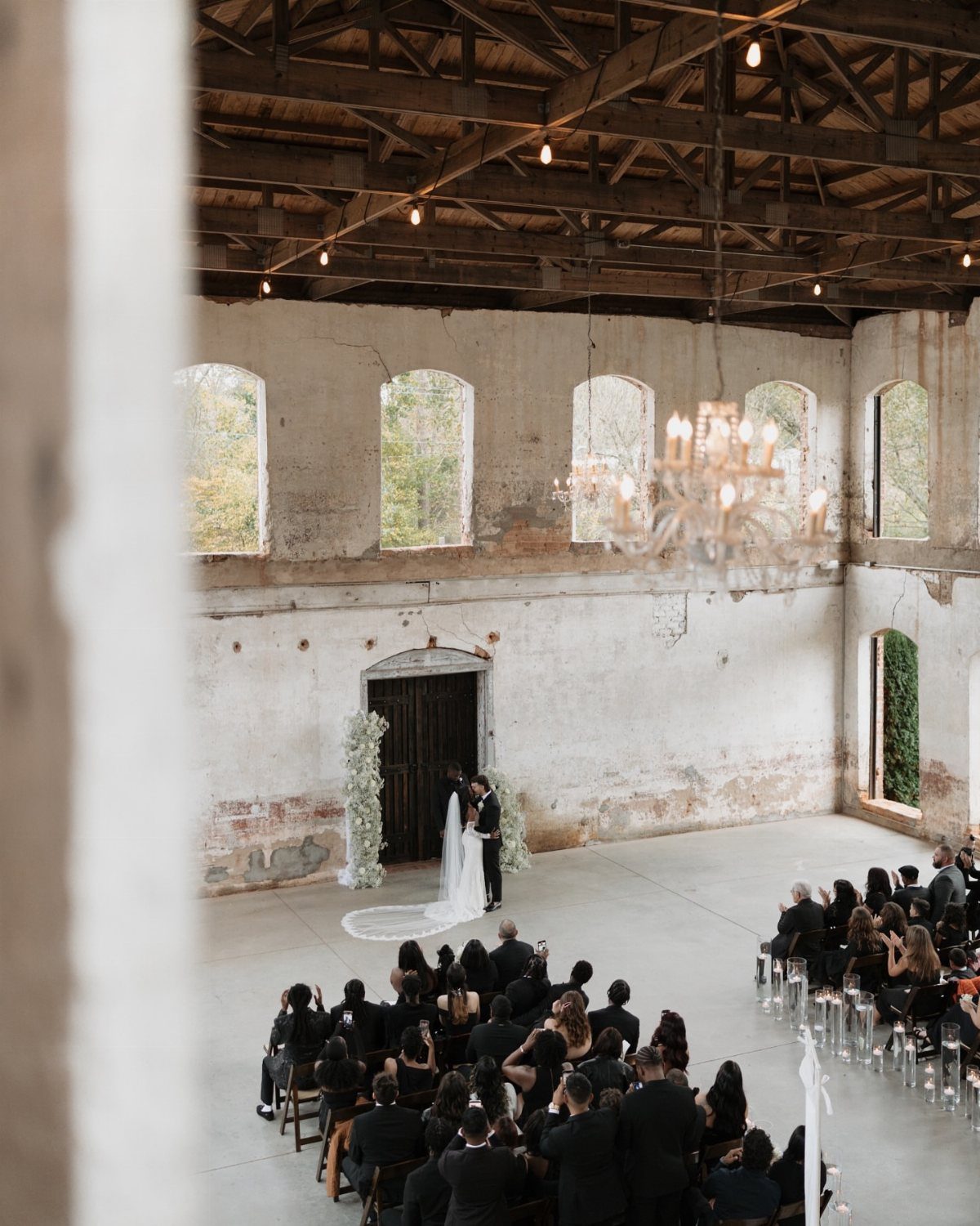 A wedding ceremony held inside a large, rustic historic mill with high ceilings and arched windows.