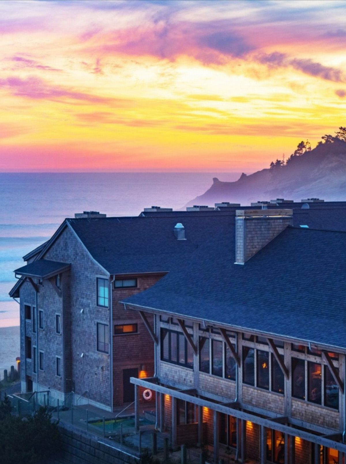 A large wooden lodge overlooking the ocean under a vibrant sunset sky.