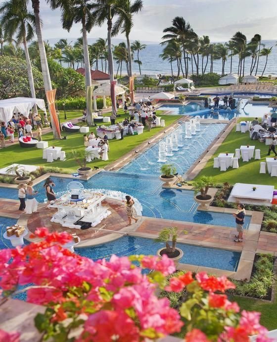 A luxury resort with swimming pools, palm trees, and guests gathered for an outdoor event.