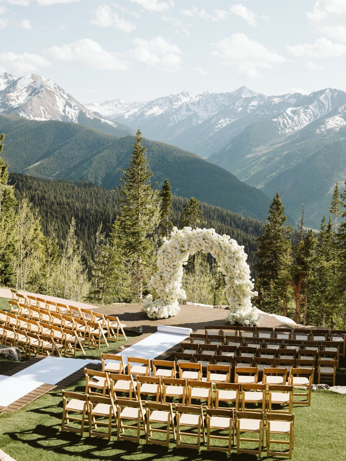 Wedding ceremony setup with gold chairs and floral arch overlooking vast mountains.