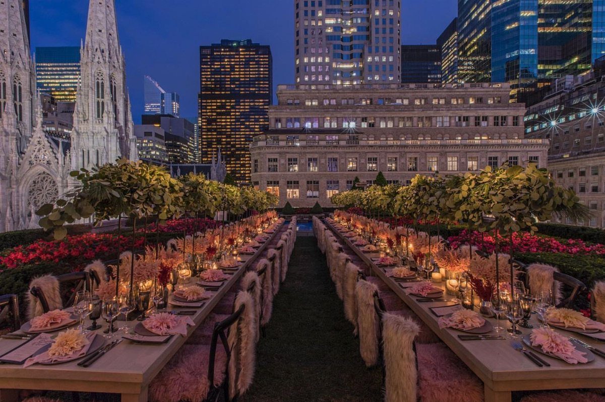 Two long dining tables set with pink flowers on a Manhattan rooftop garden at night.