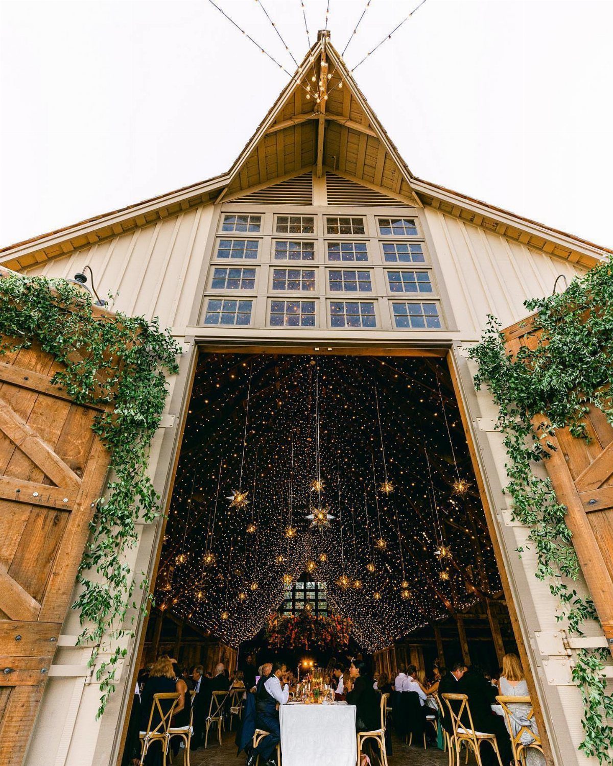 Large wooden barn with open doors revealing a festive event space decorated with twinkling fairy lights.