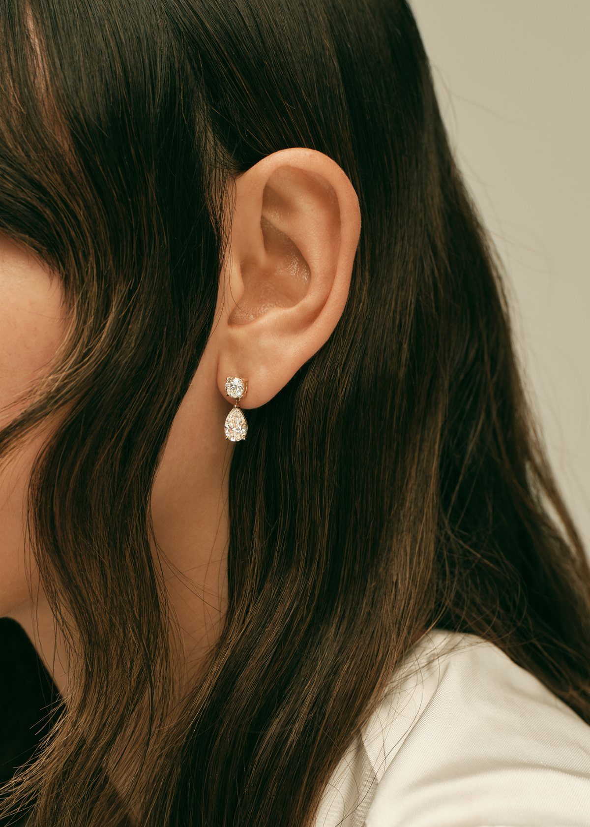 A person wearing silver earrings with a round stud and a teardrop gemstone.