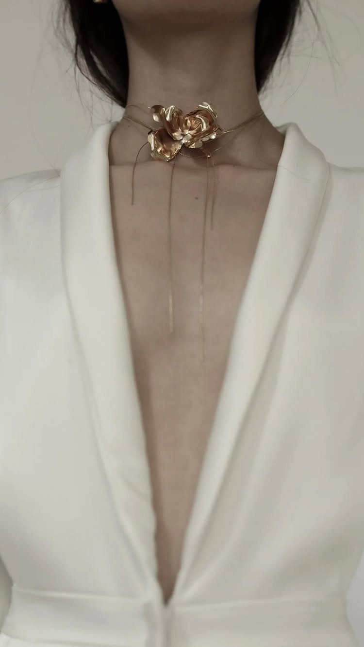A person wearing a gold rose choker necklace with a white plunging neckline top.