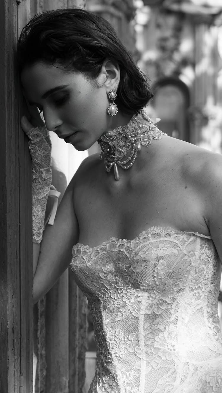 A woman wearing a pearl statement choker and pearl earrings while leaning against a wooden door.