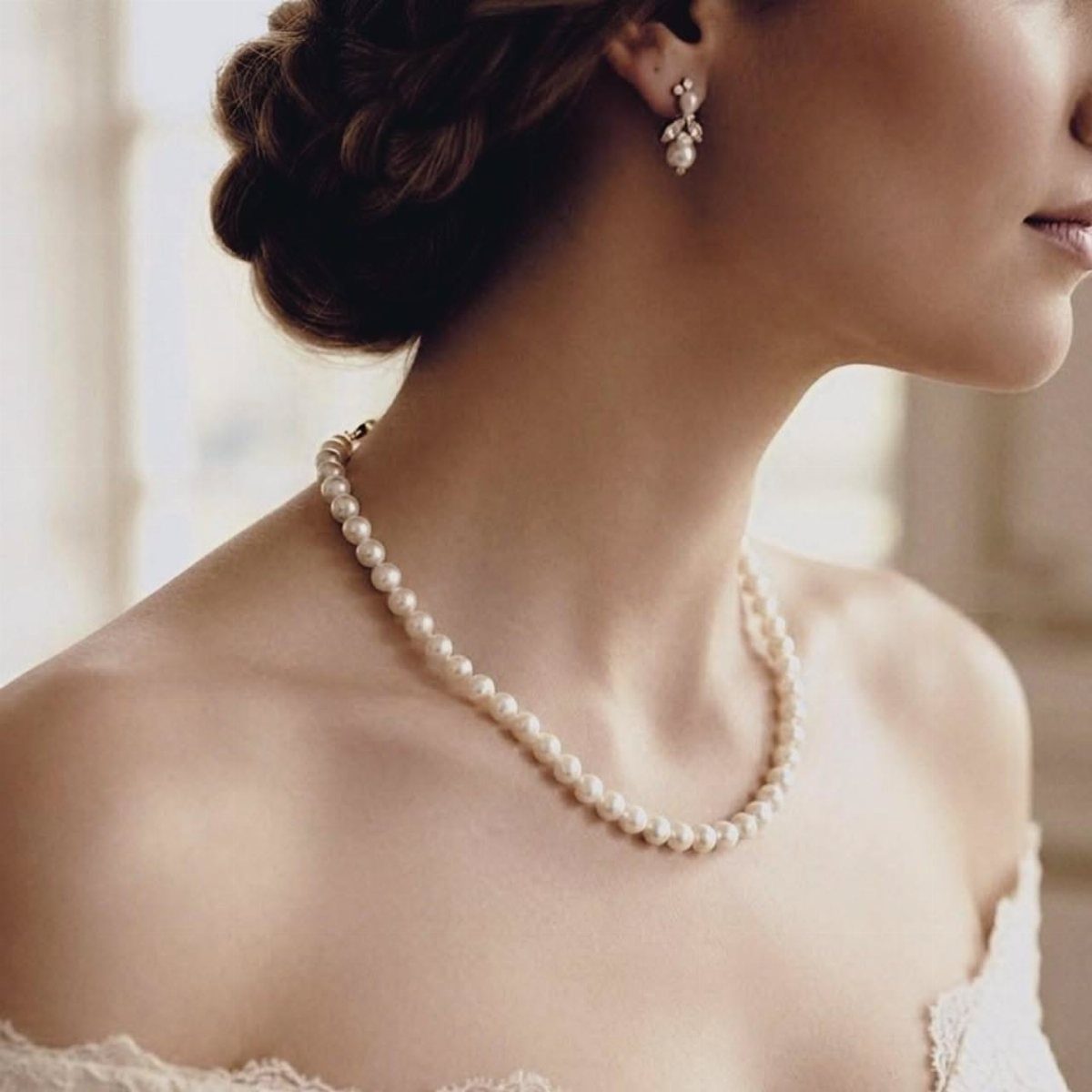 A woman wearing a simple pearl necklace and matching pearl drop earrings.