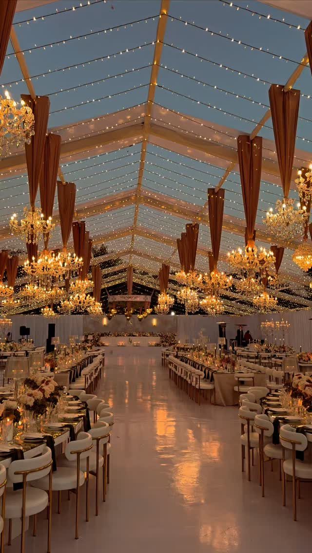 7 Long Table Wedding Reception Ideas for Outdoor Celebrations 3 Crystal chandeliers and fairy lights hanging from a clear marquee tent over wedding reception tables.