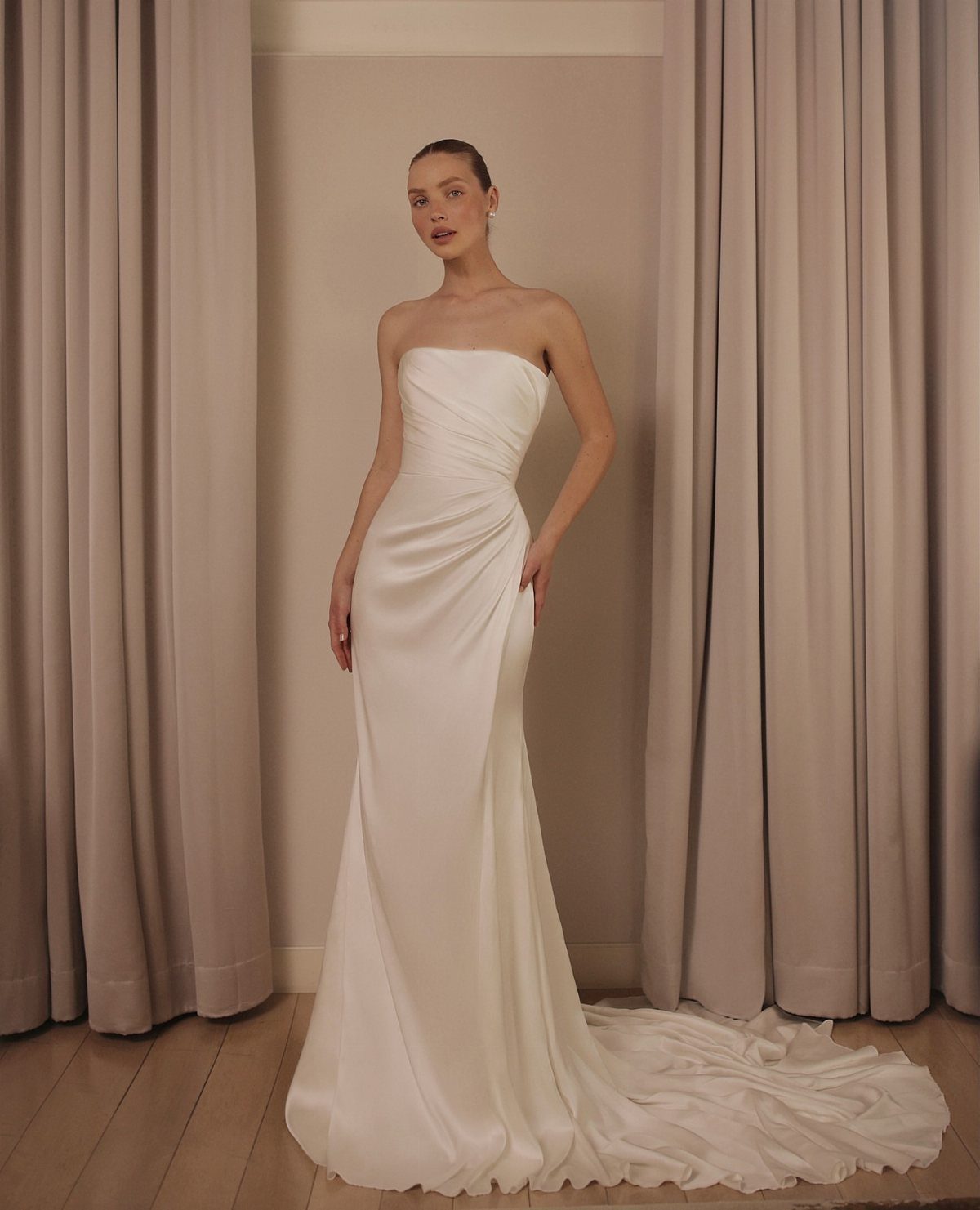 A woman wearing a strapless white silk sheath wedding gown with a long train.