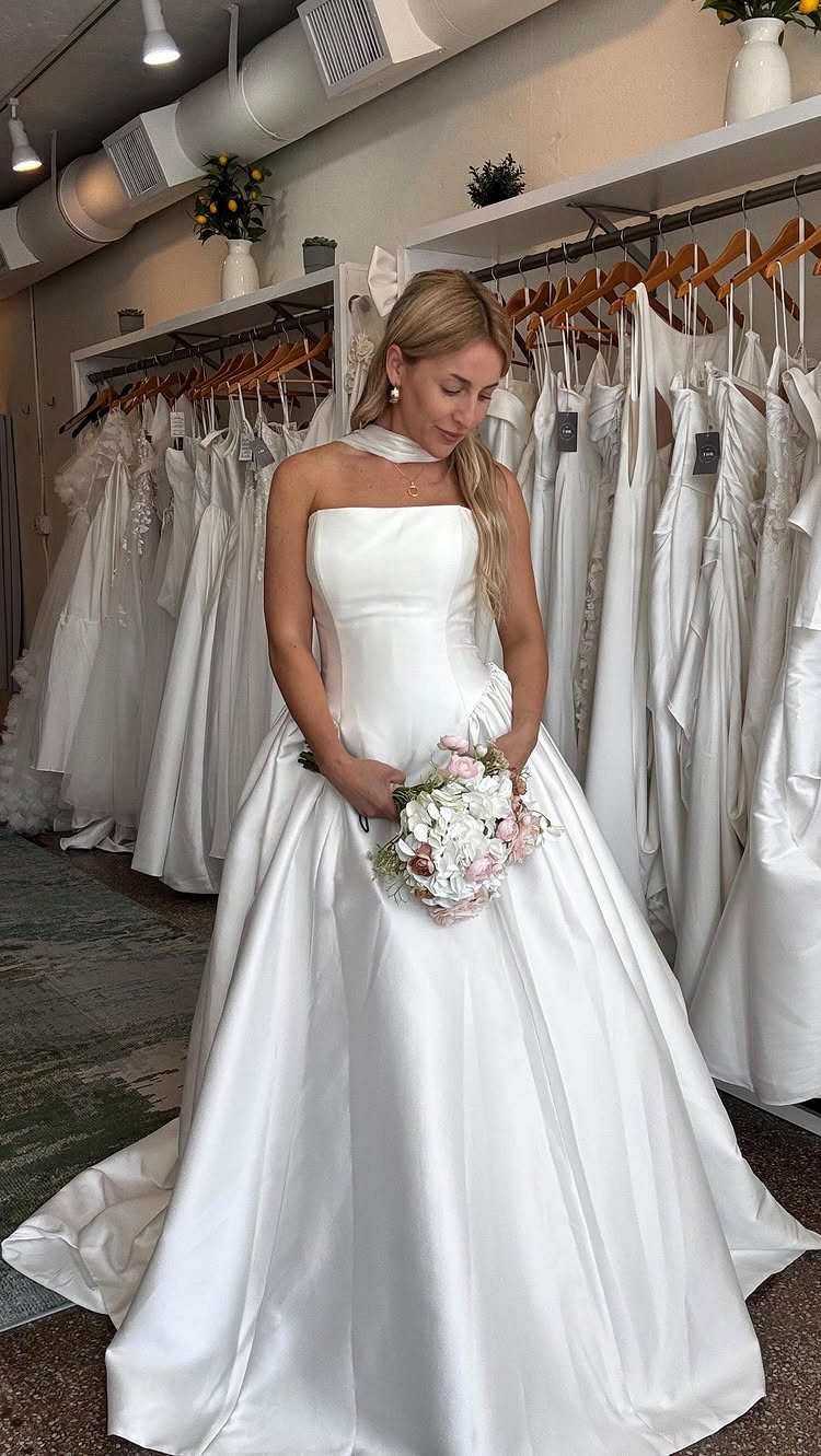 A woman in a white structured satin wedding gown holding a floral bouquet.