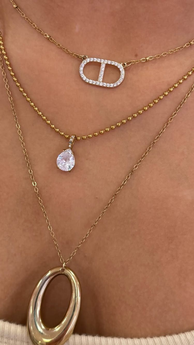 Three layered gold necklaces with various pendants worn on a person's neck.