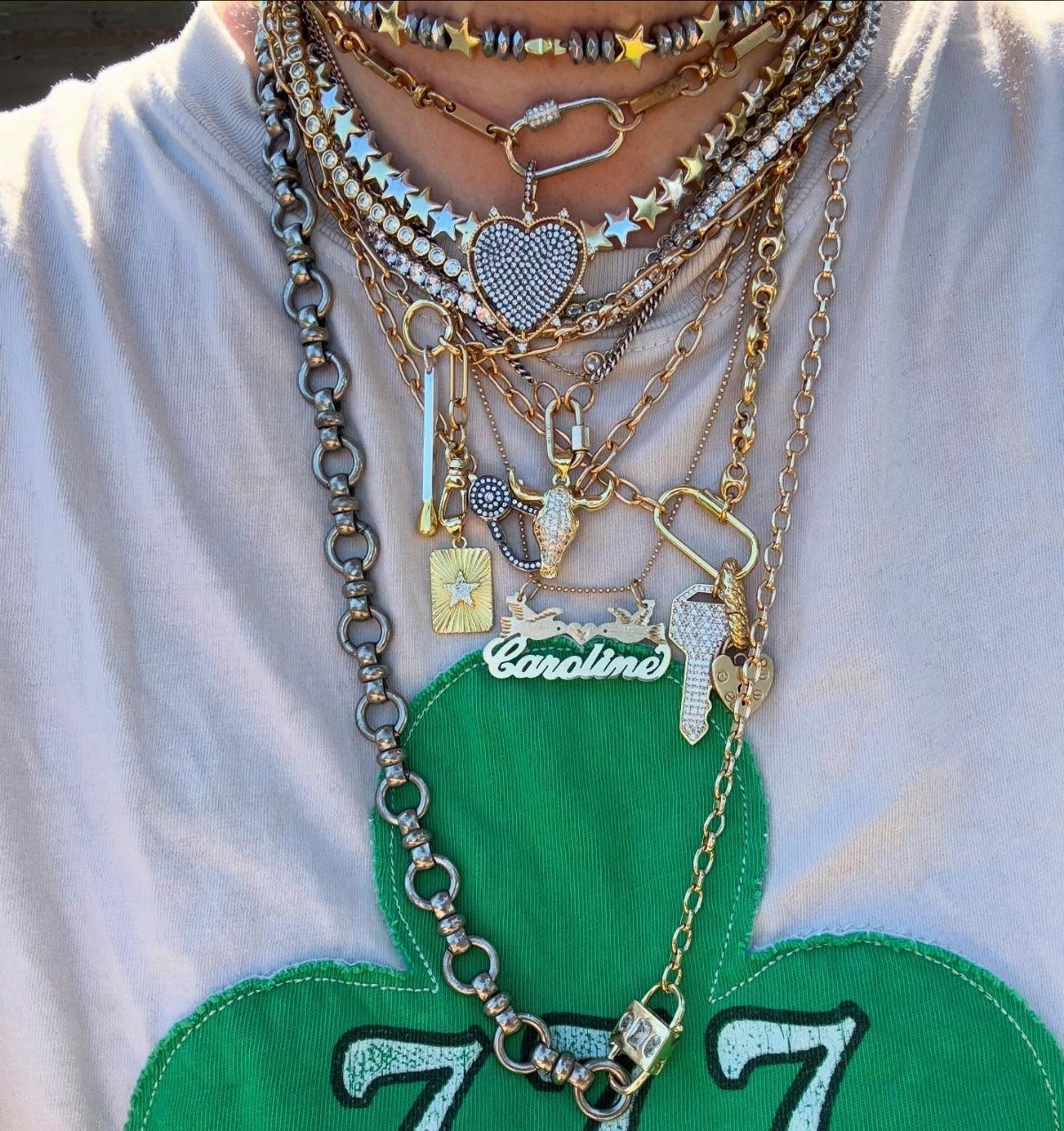 Multiple layered gold and silver necklaces with various charms worn over a white t-shirt.
