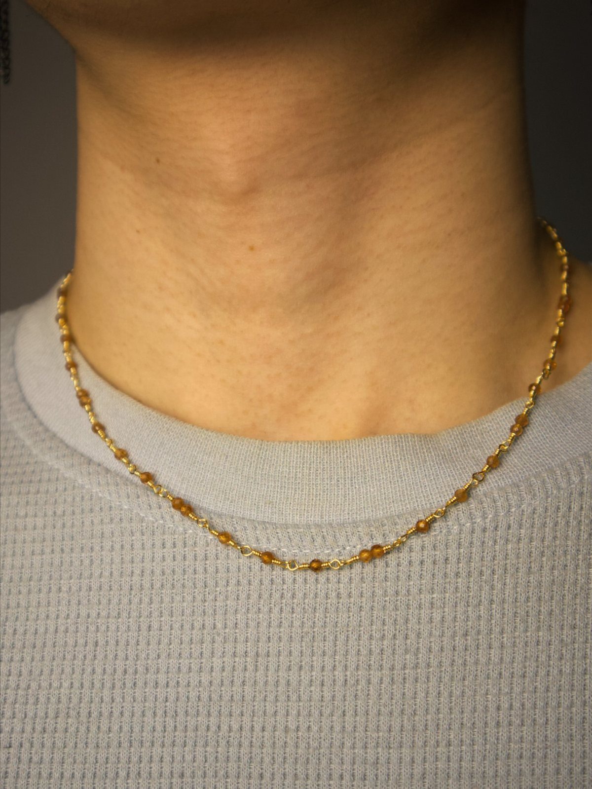 Precious Stones Jewelry: 11 Ideas From Emerald to Gold Bangles 8 A person wearing a thin gold necklace with small amber-colored gemstones around their neck.