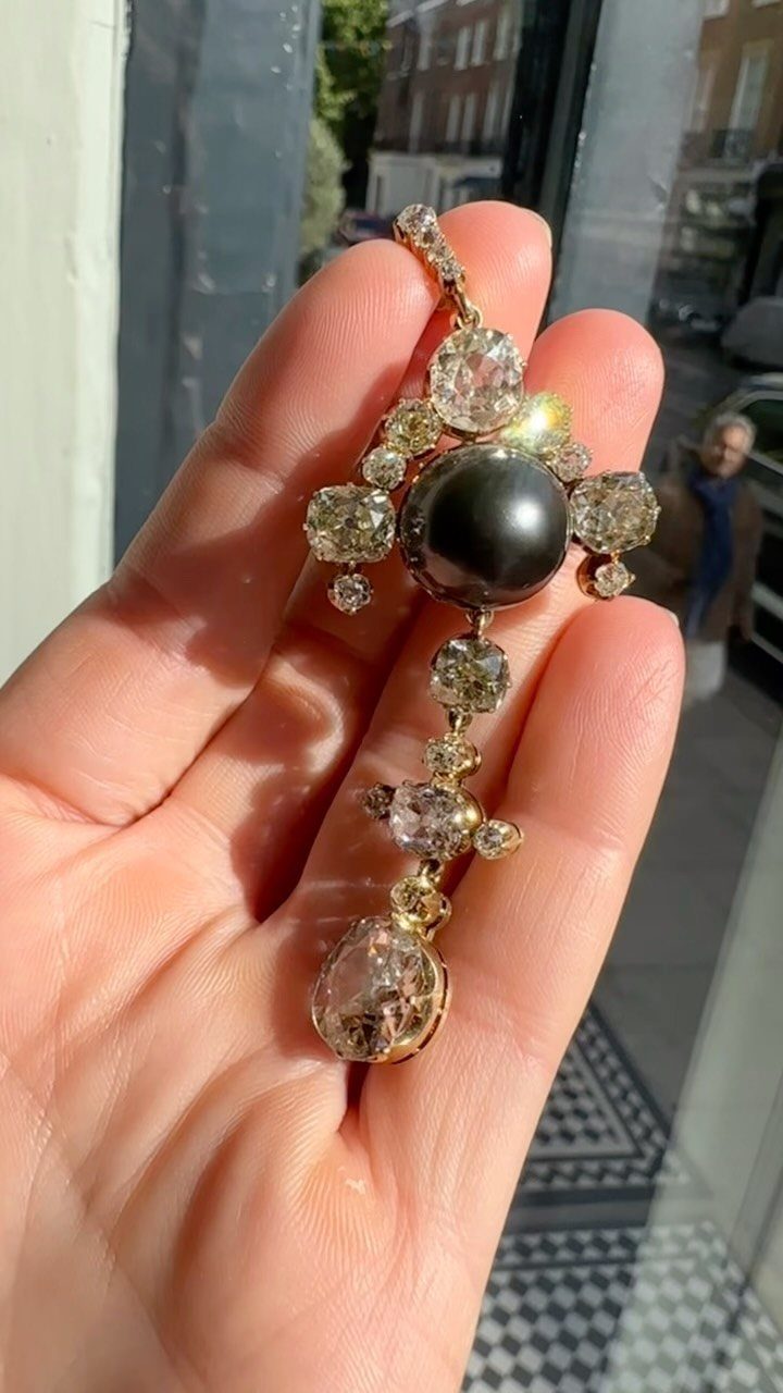Precious Stones Jewelry: 11 Ideas From Emerald to Gold Bangles 5 A hand holding a gold pendant with a large black pearl and clear gemstones.