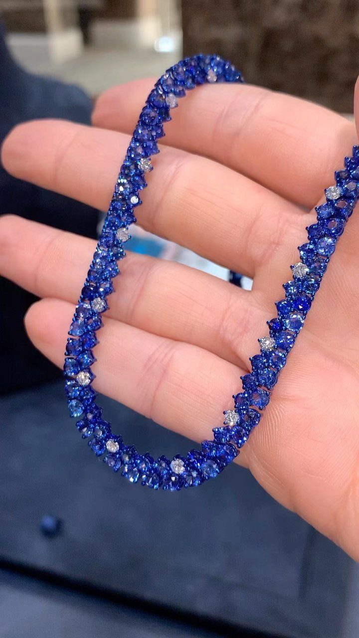 Precious Stones Jewelry: 11 Ideas From Emerald to Gold Bangles 2 A hand holding a brilliant blue sapphire gemstone necklace against a blurred background.