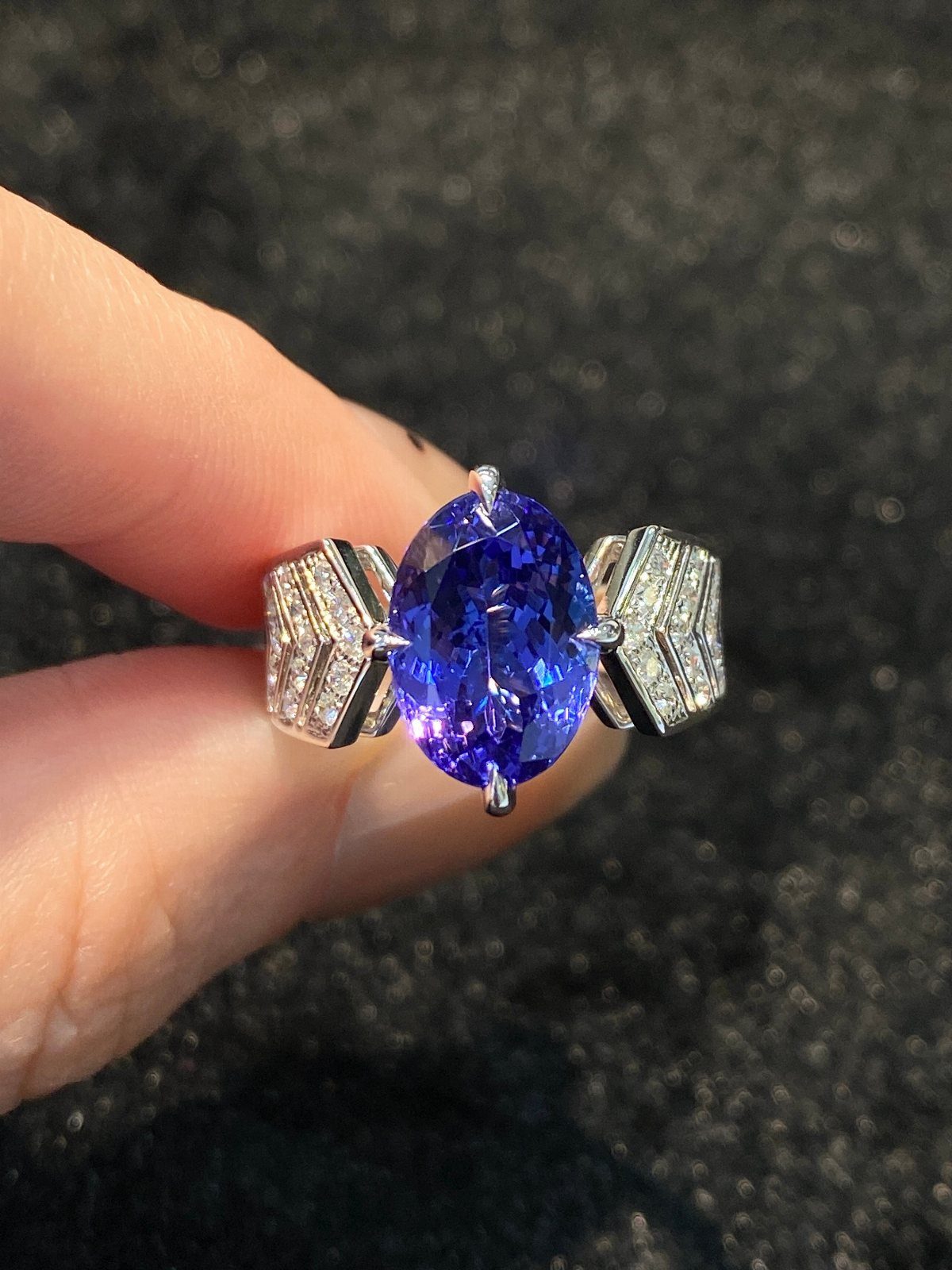 Precious Stones Jewelry: 11 Ideas From Emerald to Gold Bangles 7 A large oval blue gemstone ring held between two fingers against a dark background.