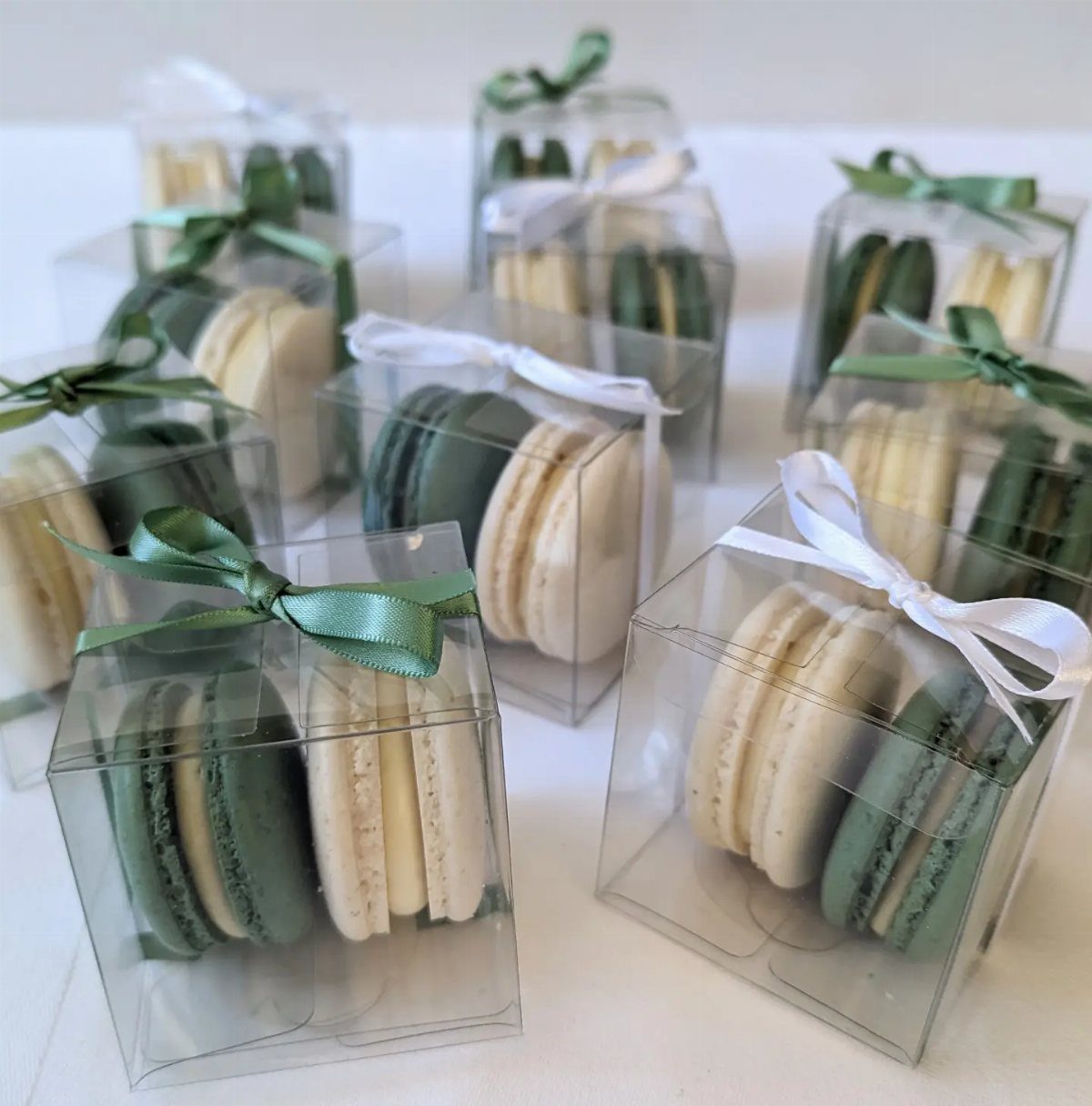 Rehearsal Dinner Gift Ideas: 9 Ways to Thank Your People 8 Clear plastic favor boxes containing white and green macarons tied with satin ribbons on a white surface.