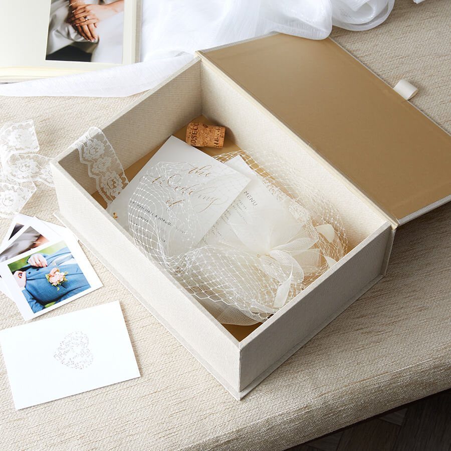 Rehearsal Dinner Gift Ideas: 9 Ways to Thank Your People 2 An open cream storage box filled with wedding keepsakes and lace next to scattered photographs.