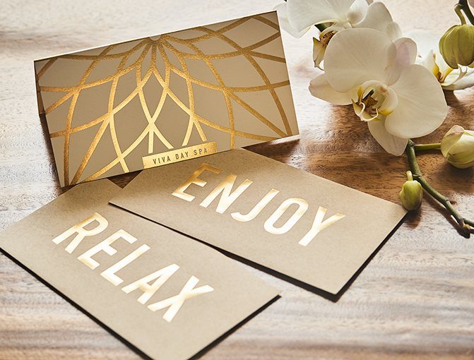 Rehearsal Dinner Gift Ideas: 9 Ways to Thank Your People 4 Gold foil gift cards reading Relax and Enjoy next to white orchids on wood.