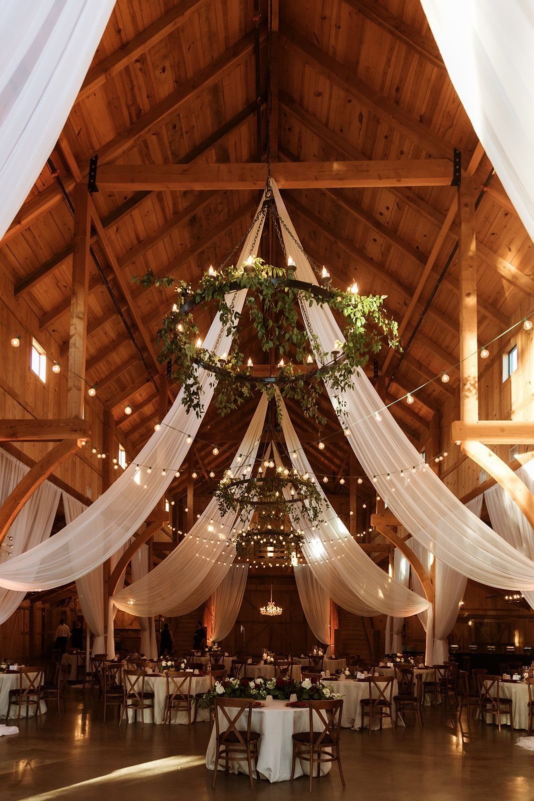 A decorated wooden barn interior with white fabric draping and wedding tables set for a reception.
