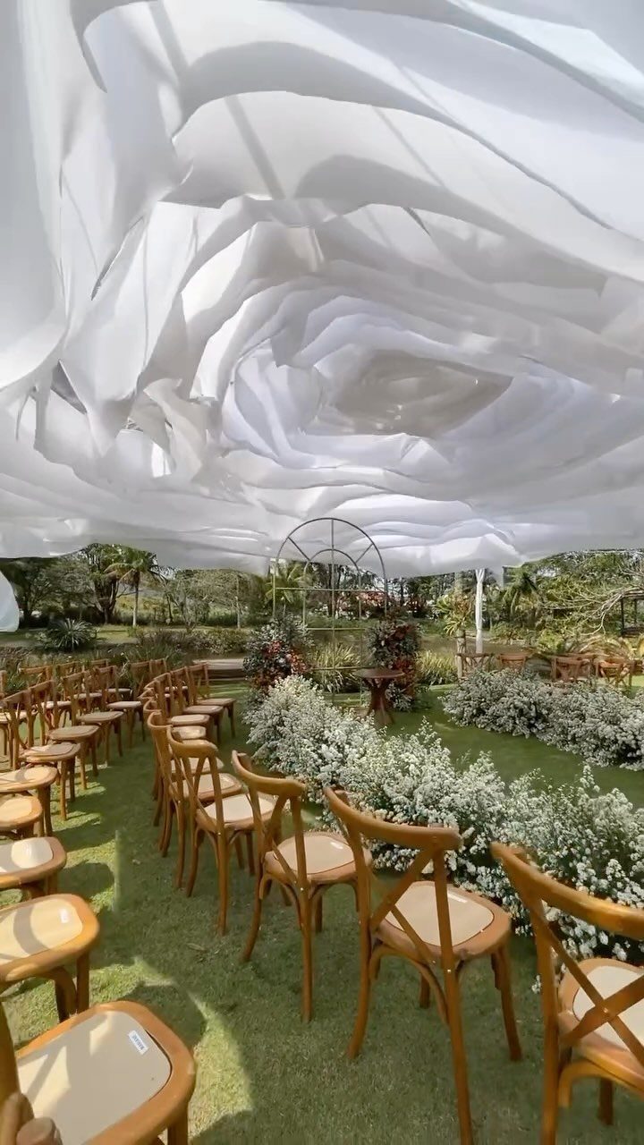 Wooden chairs arranged for an outdoor wedding ceremony under a large white fabric canopy.