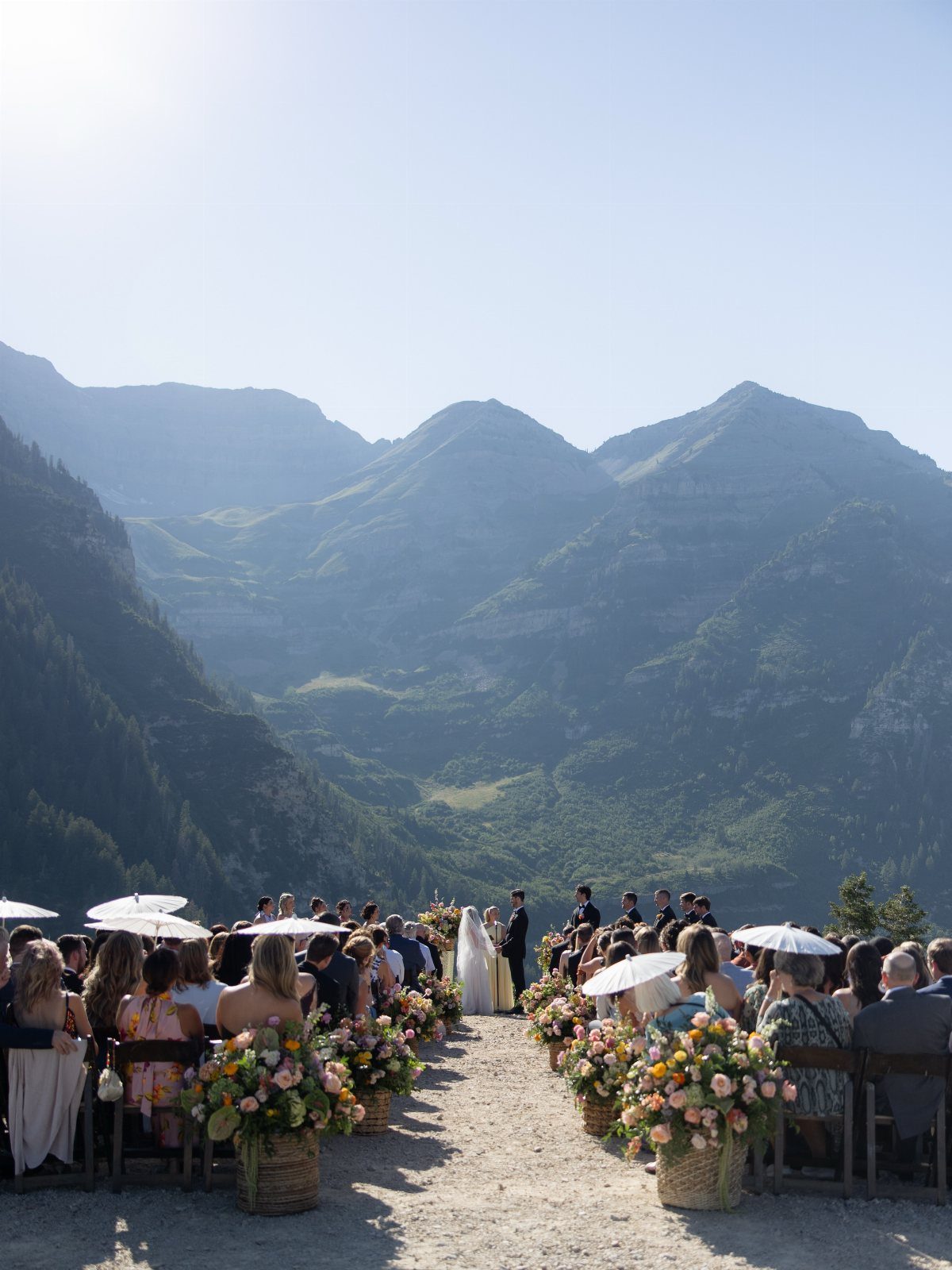Wedding guests seated on a hilltop overlooking a vast mountain range during an outdoor ceremony.