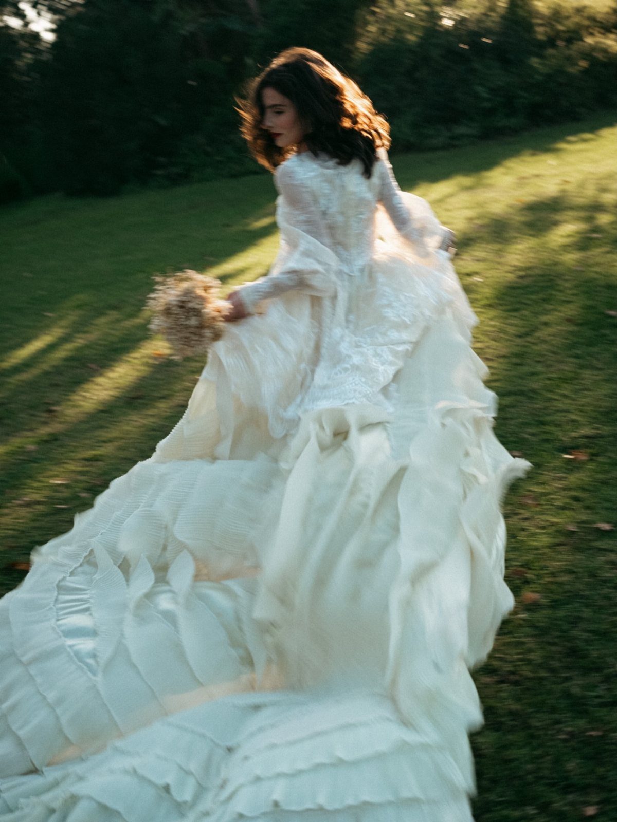 A woman in a flowing lace wedding dress running through a sunlit grassy field.
