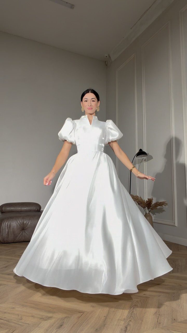 A woman posing in a voluminous white satin wedding dress with puffed sleeves.