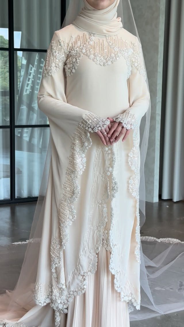 A person wearing a cream long-sleeved wedding dress with intricate lace and beadwork details.