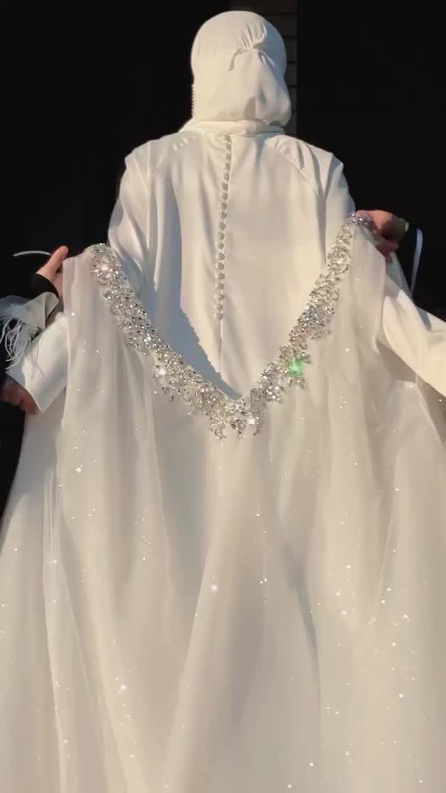 A person wearing a white flowing wedding dress with a sparkling crystal-embellished cape.