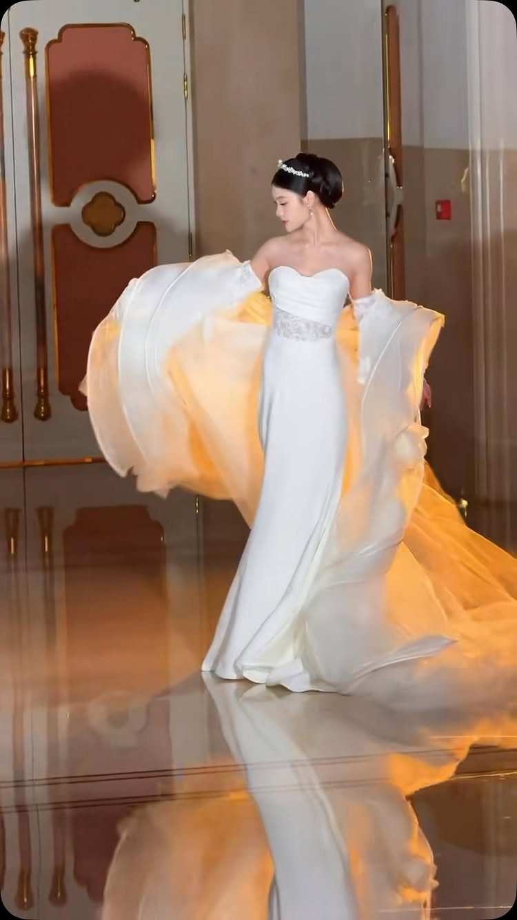 Woman in a white strapless wedding dress with a large, flowing, voluminous train walking indoors.