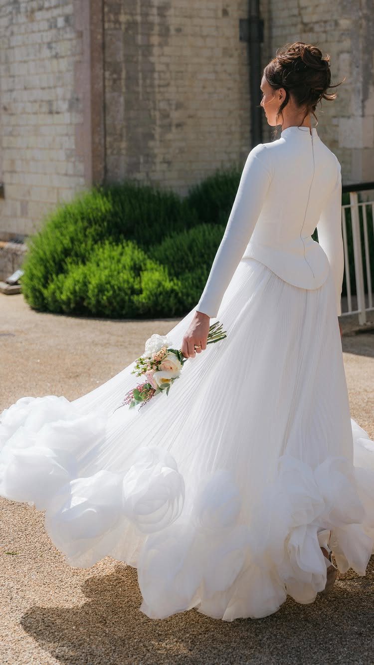 Woman in a white long-sleeved wedding dress walking with a voluminous ruffled skirt.