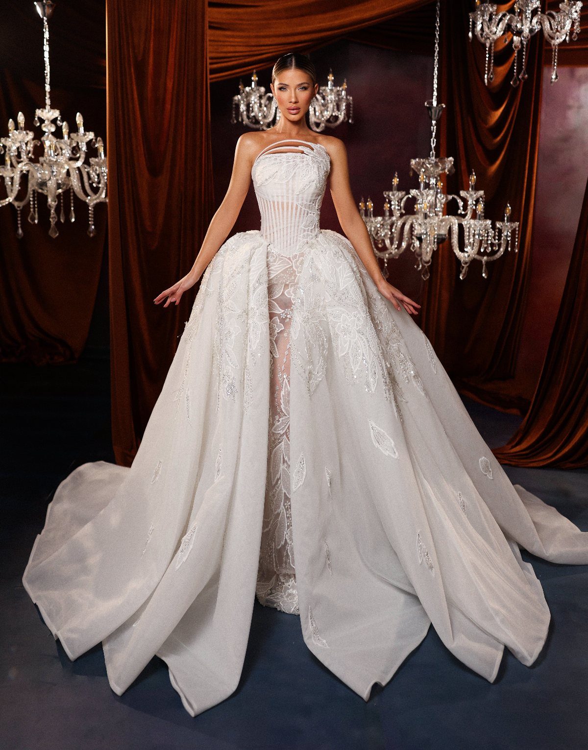 Wedding Dress with Overskirt: 5 Styles to Consider 4 Woman wearing a white wedding dress with a voluminous, floral embroidered overskirt and crystal chandeliers.