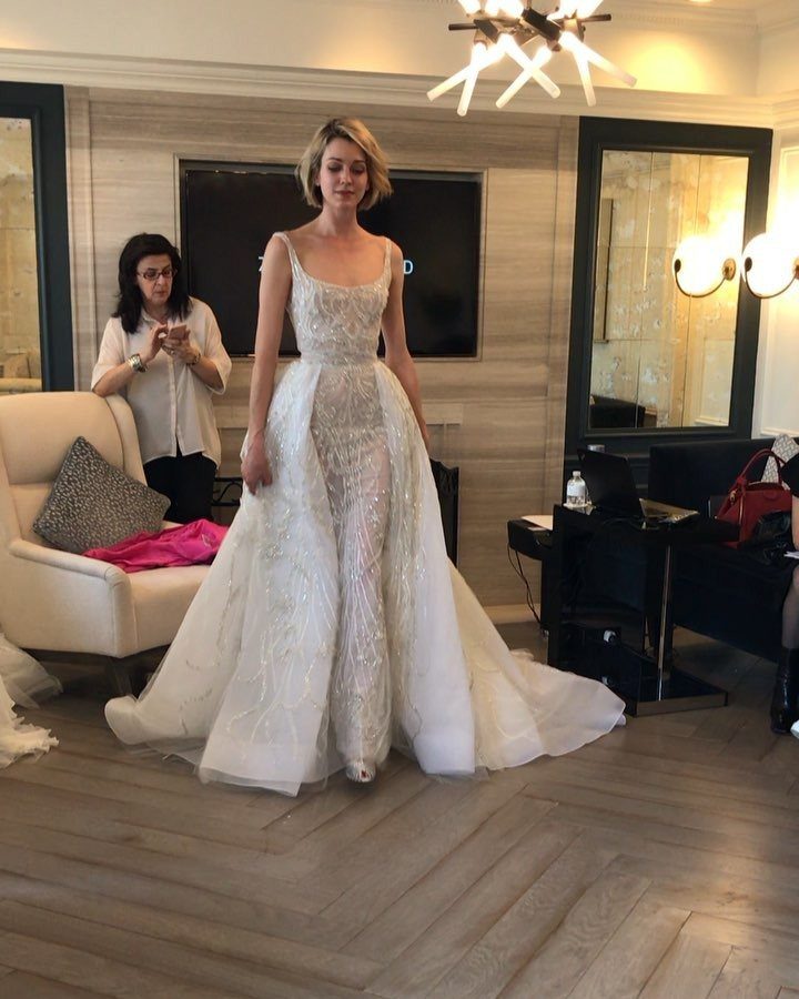 Wedding Dress with Overskirt: 5 Styles to Consider 5 A woman wearing a white embroidered wedding dress with a voluminous layered overskirt.