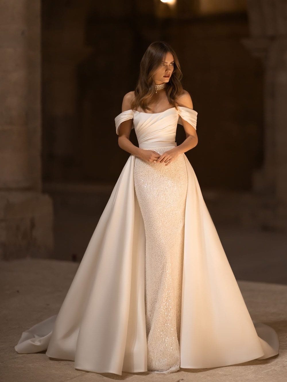 Wedding Dress with Overskirt: 5 Styles to Consider 3 Woman in an off-the-shoulder wedding dress with a voluminous white satin overskirt.