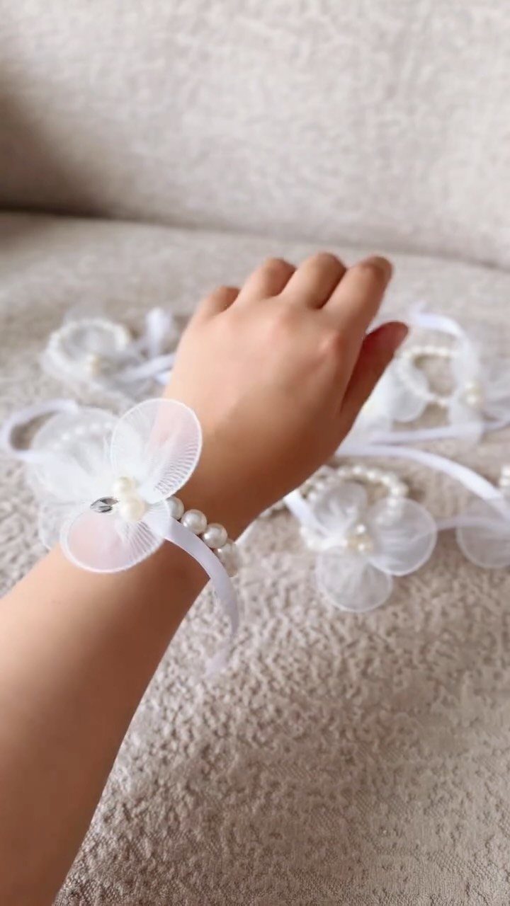 Wedding Dress with Pearl Necklace: 5 Styling Ideas That Work 4 A hand wearing a white pearl bracelet with a sheer fabric flower decoration on a textured surface.