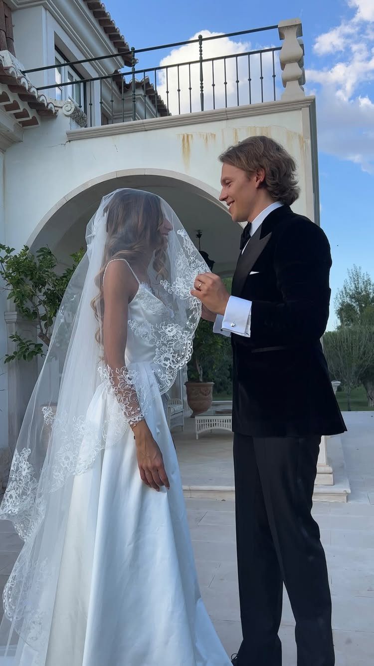 A bride in a white lace wedding dress wearing a lace blusher veil covering her face.