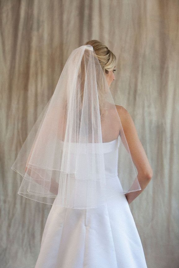 A bride wearing a white wedding dress and a layered elbow length tulle veil.