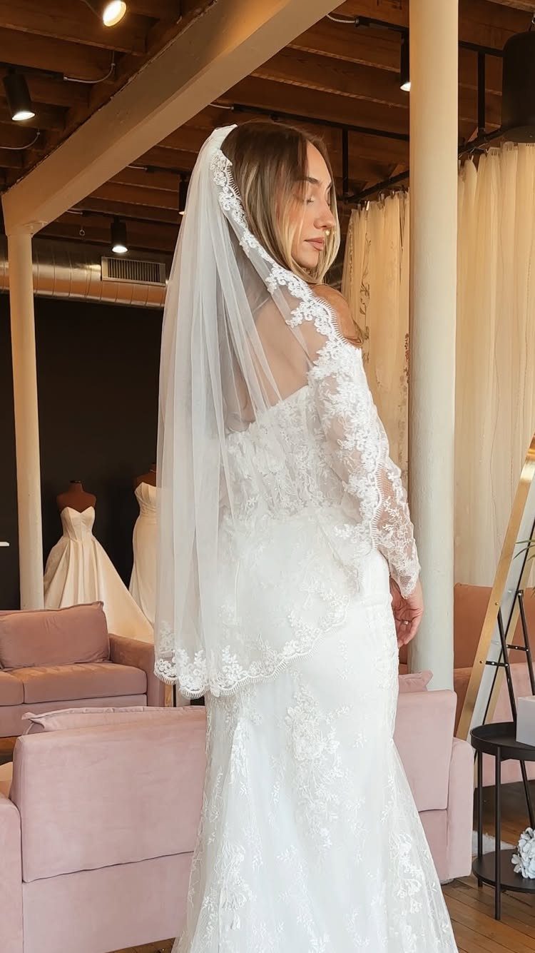 A woman wearing a white lace wedding dress and a sheer fingertip length veil.