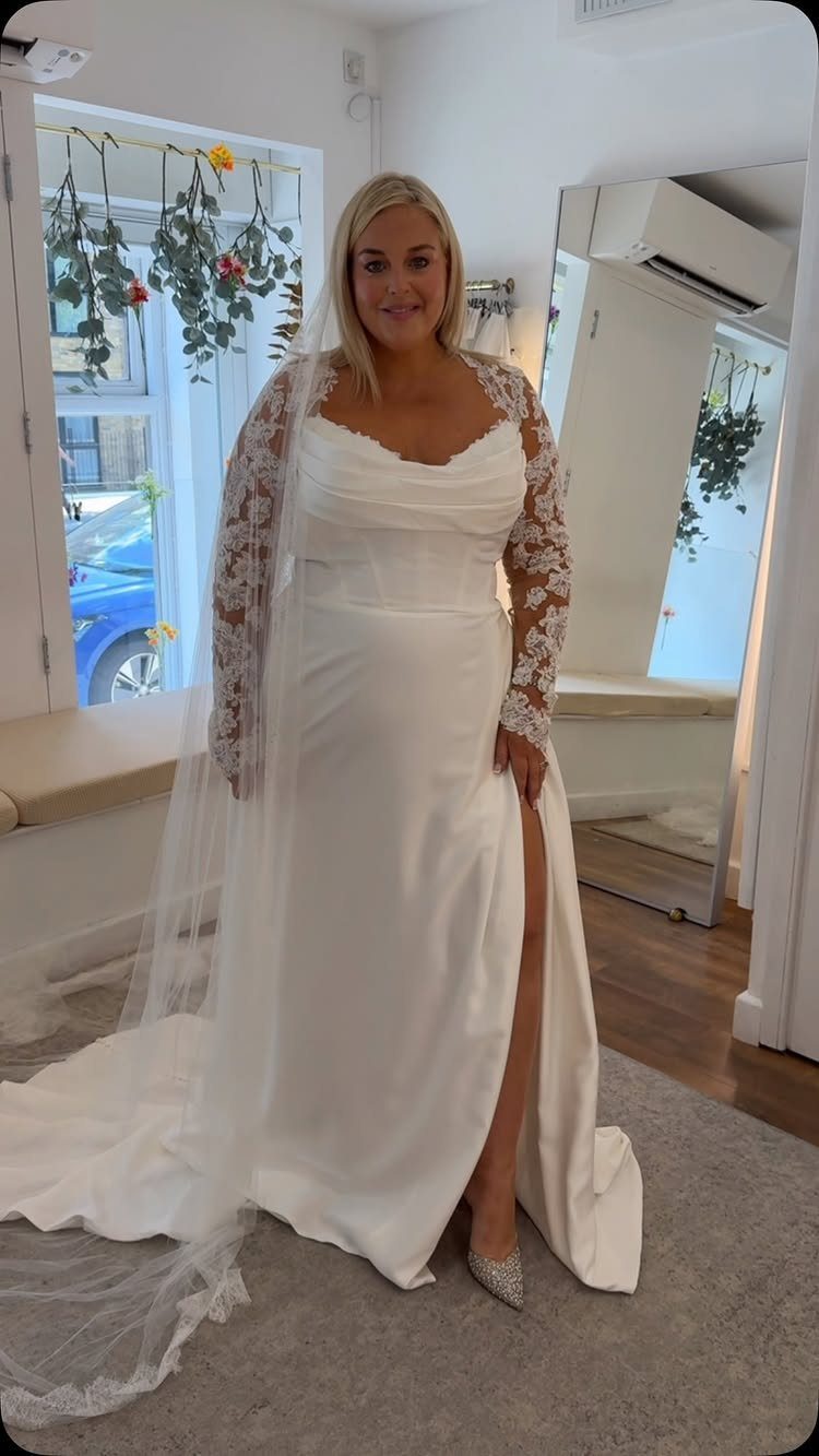 Blonde woman wearing a white satin wedding dress with lace sleeves and a long sheer veil.